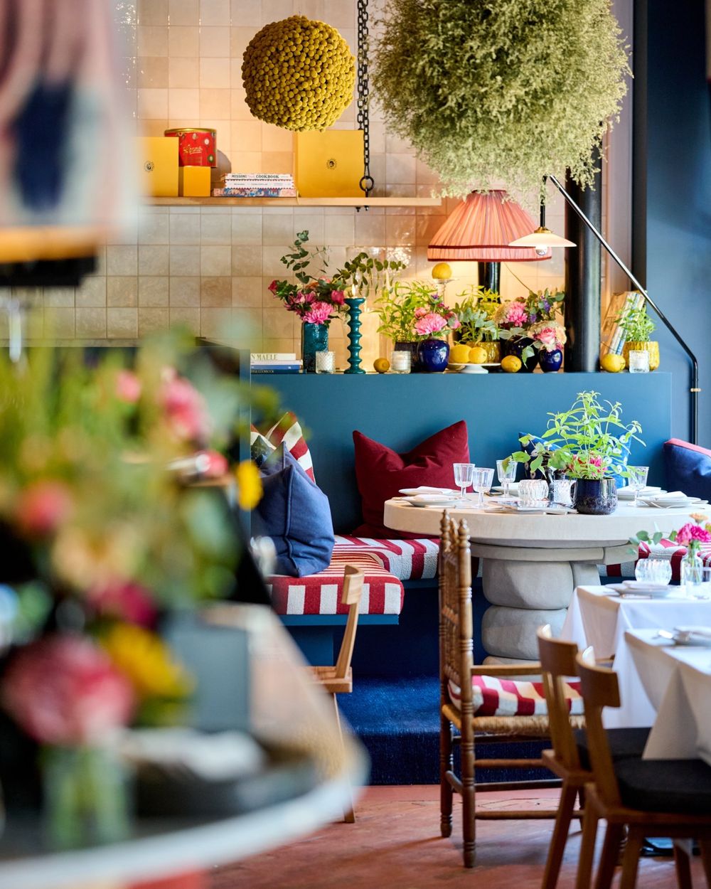 La salle avec la banquette bleue, les coussins rayés et des fleurs fraîches