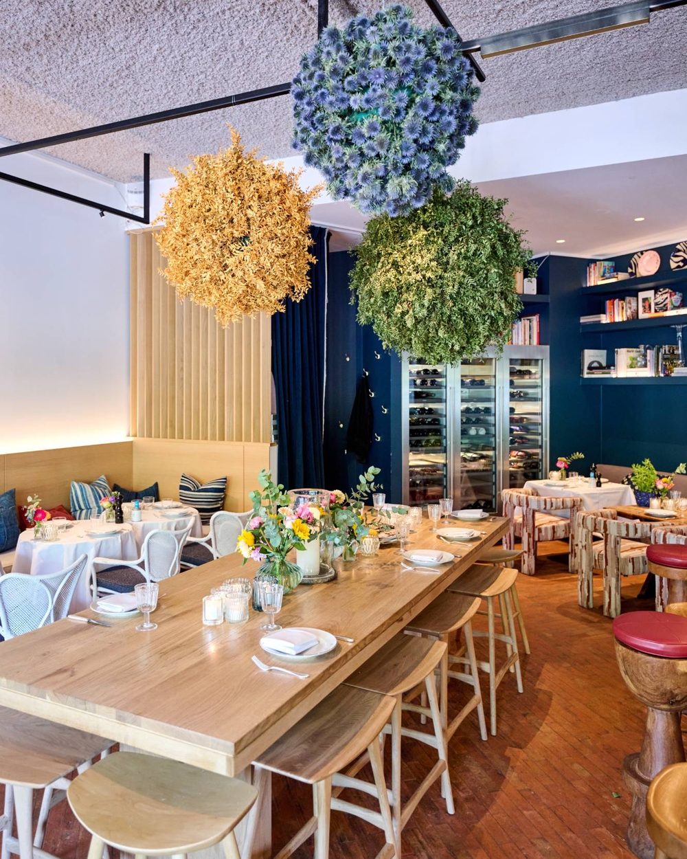La longue table en bois sous les boules de fleurs, avec les caves à vin au fond